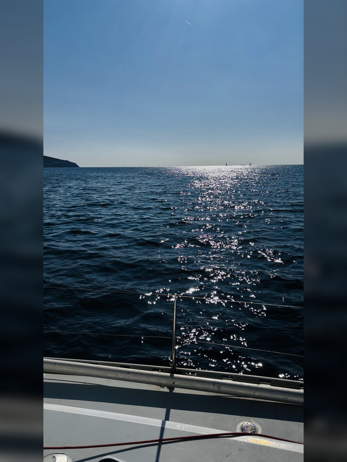 Deniz üzerinde güneş parıltısı ve ufukta yelkenliler